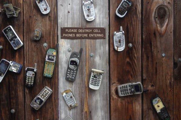 19 very old cell phones on pieces of weathered wood with a sign that says: Please Destroy Cell Phones Before Entering.