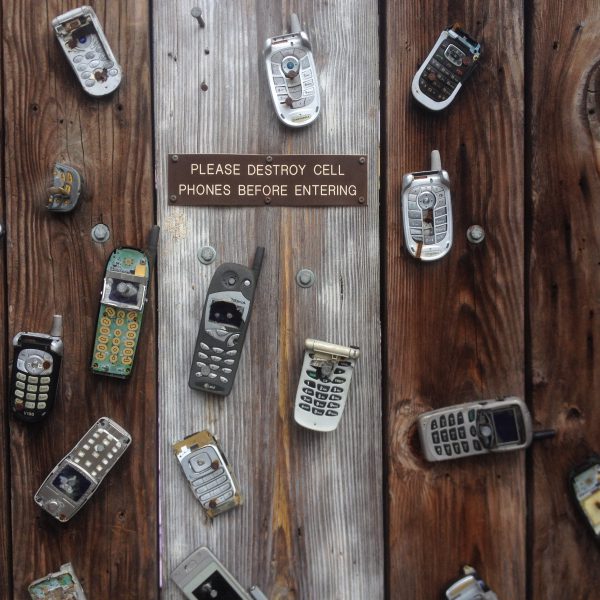 19 very old cell phones on pieces of weathered wood with a sign that says: Please Destroy Cell Phones Before Entering.